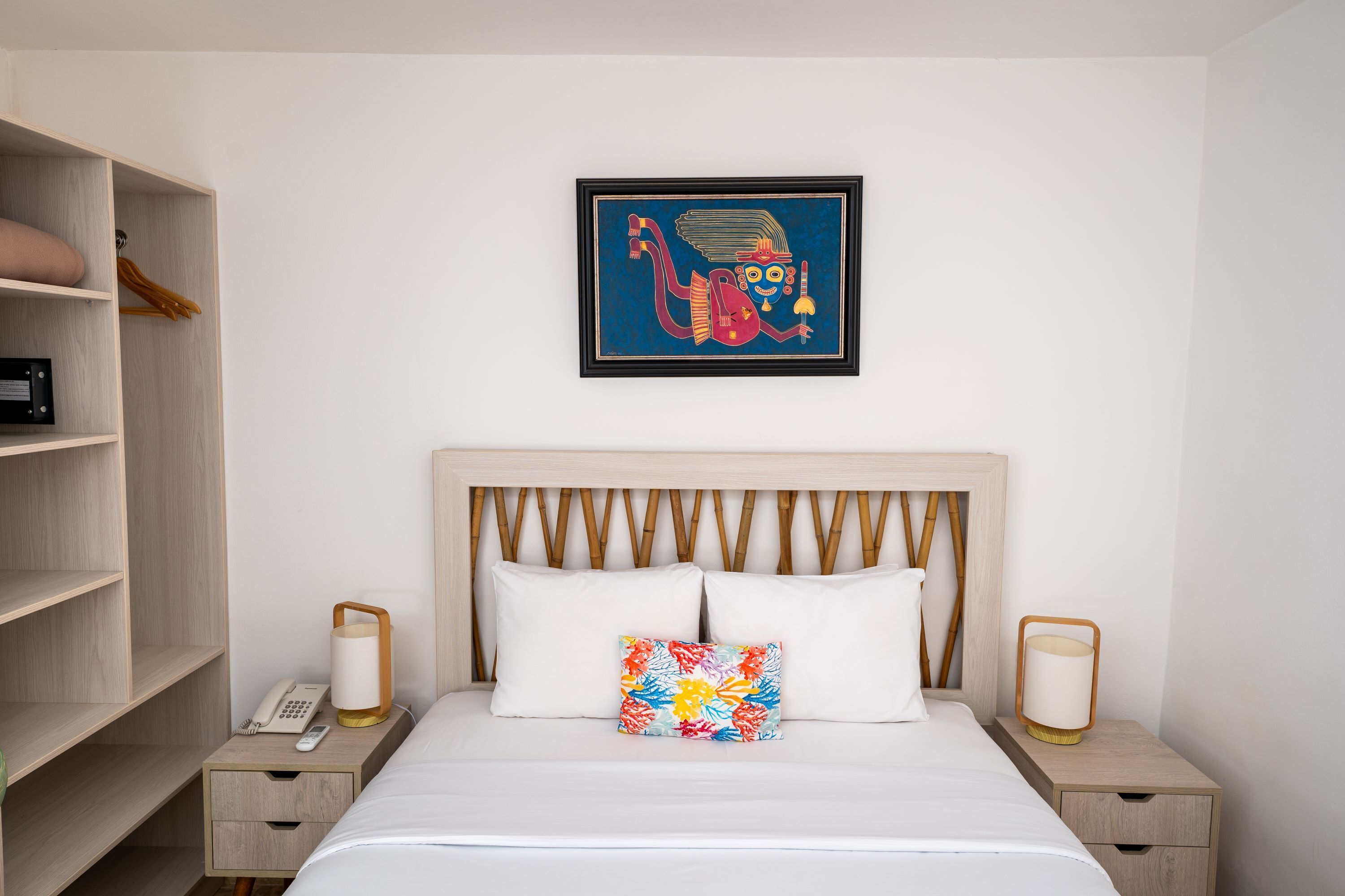 A neatly arranged hotel room with a bed, bedside tables, a lamp, a phone, and a wall-mounted artwork.