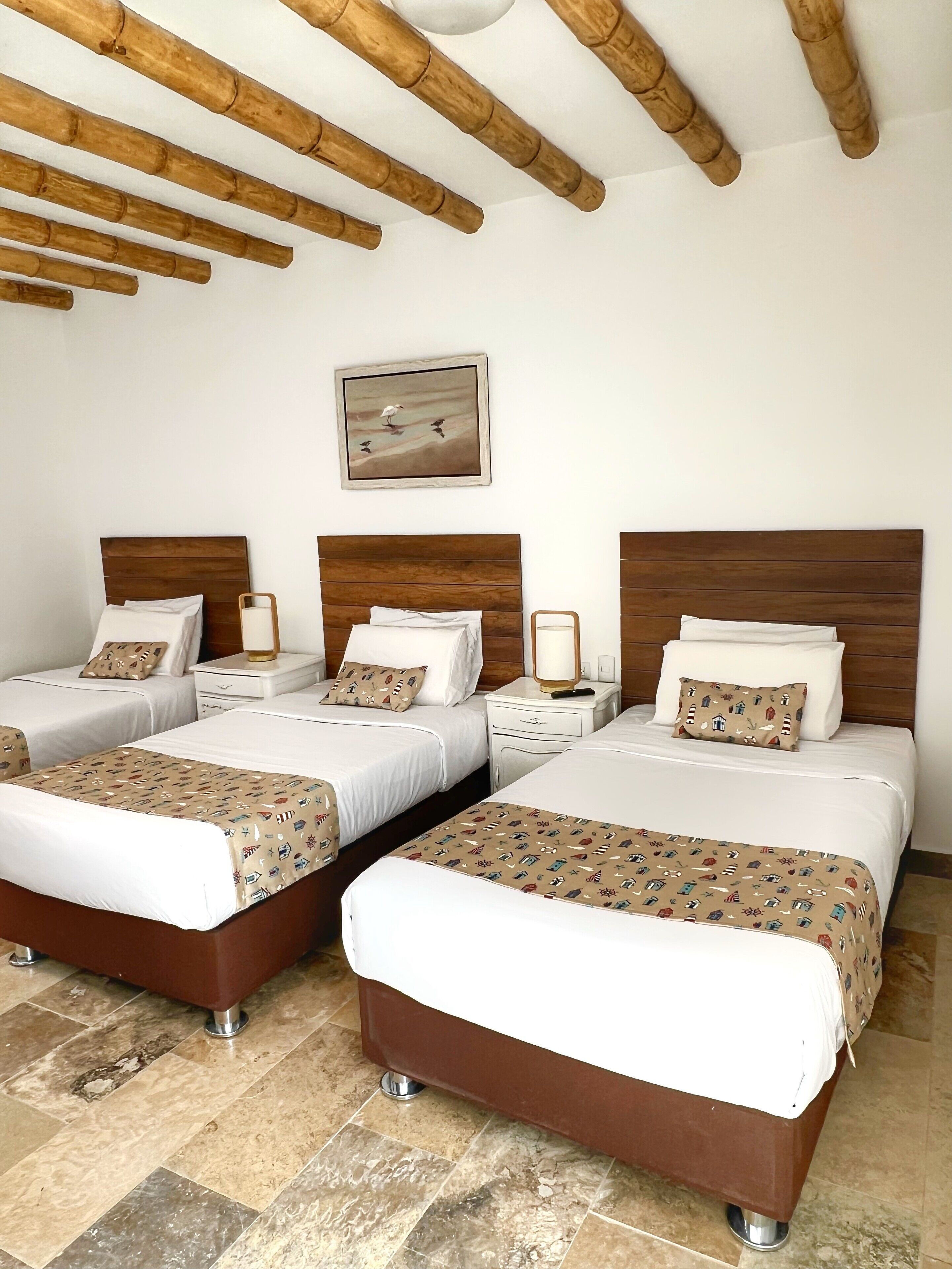 A hotel room with four beds, wooden headboards, a painting on the wall, and a tiled floor.