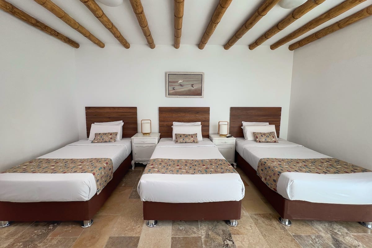 A hotel room with three beds, wooden headboards, a framed picture on the wall, and a tiled floor.