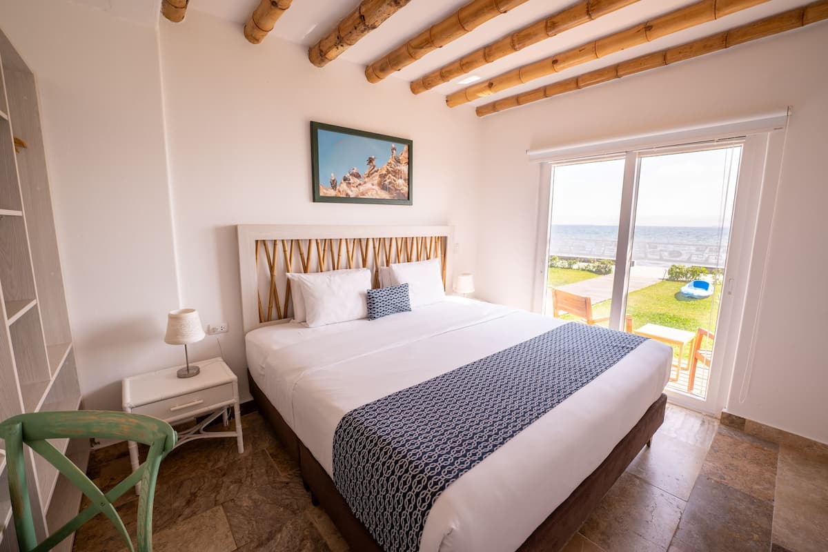 A bedroom with a bed, a nightstand, a chair, and a view of the sea through a large window.