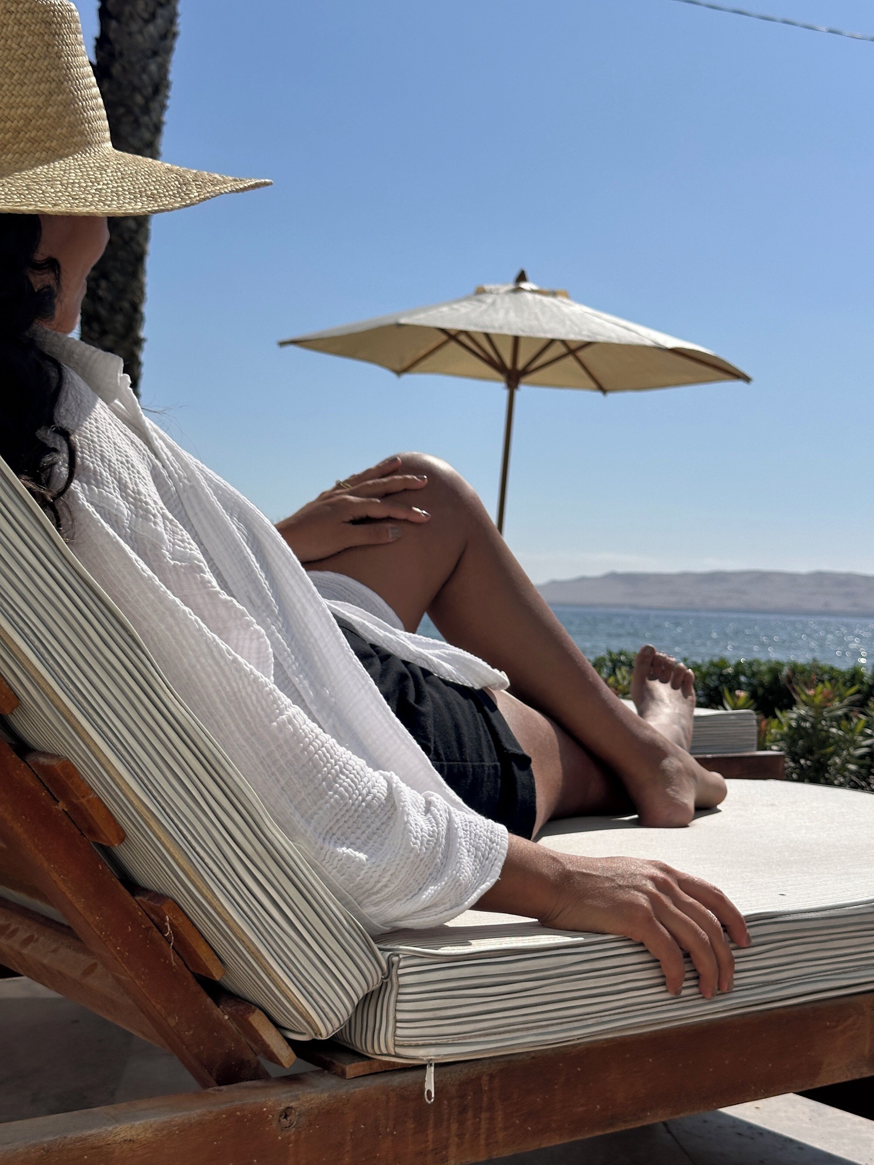 A person relaxing on a lounge chair with a view of the sea and mountains.