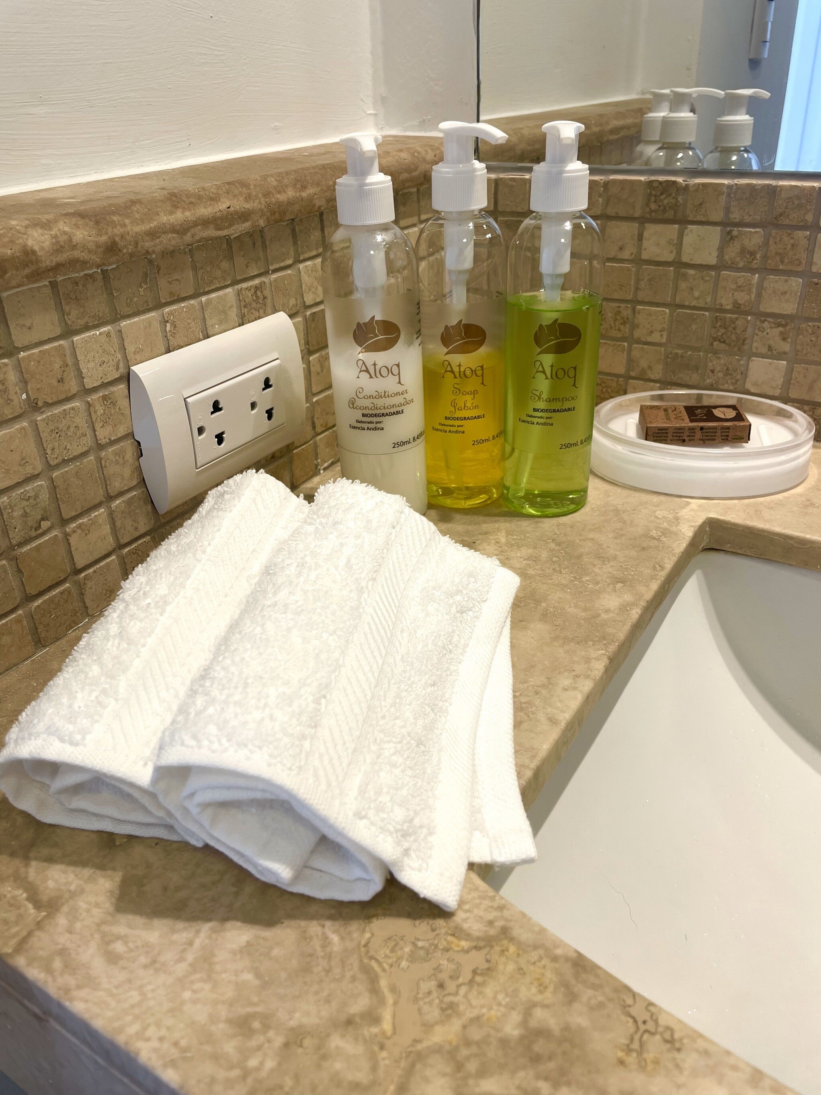 A bathroom with a towel, three bottles of Atoq products, and a soap dish.