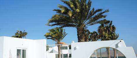 A modern villa with a white exterior, a wooden deck, and a lounge area with two chairs.