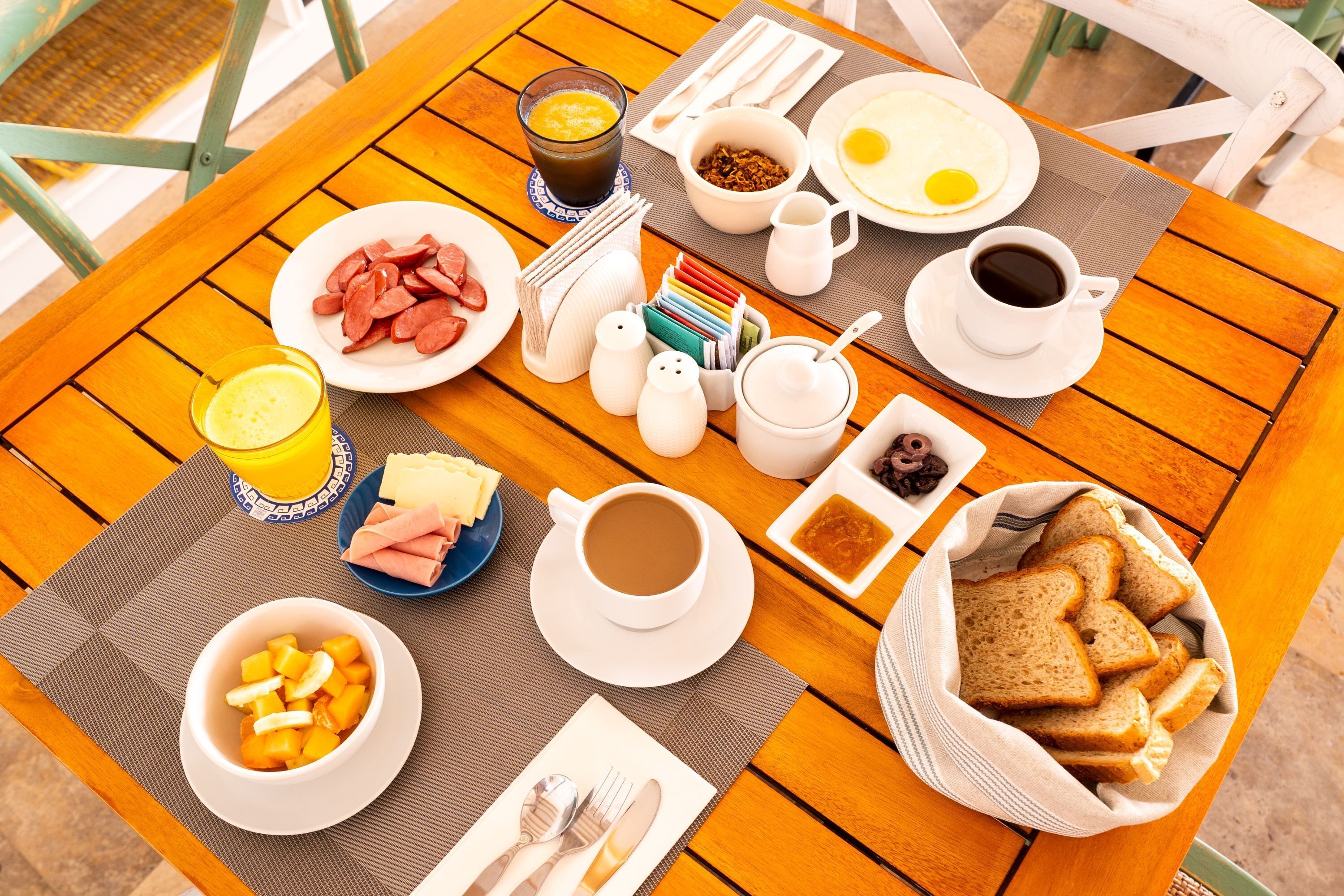 A wooden table with breakfast items including eggs, sausage, toast, and coffee.
