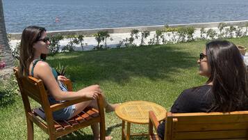 Two people seated at a small round table outdoors, with a grassy area and a view of a body of water and distant hills.