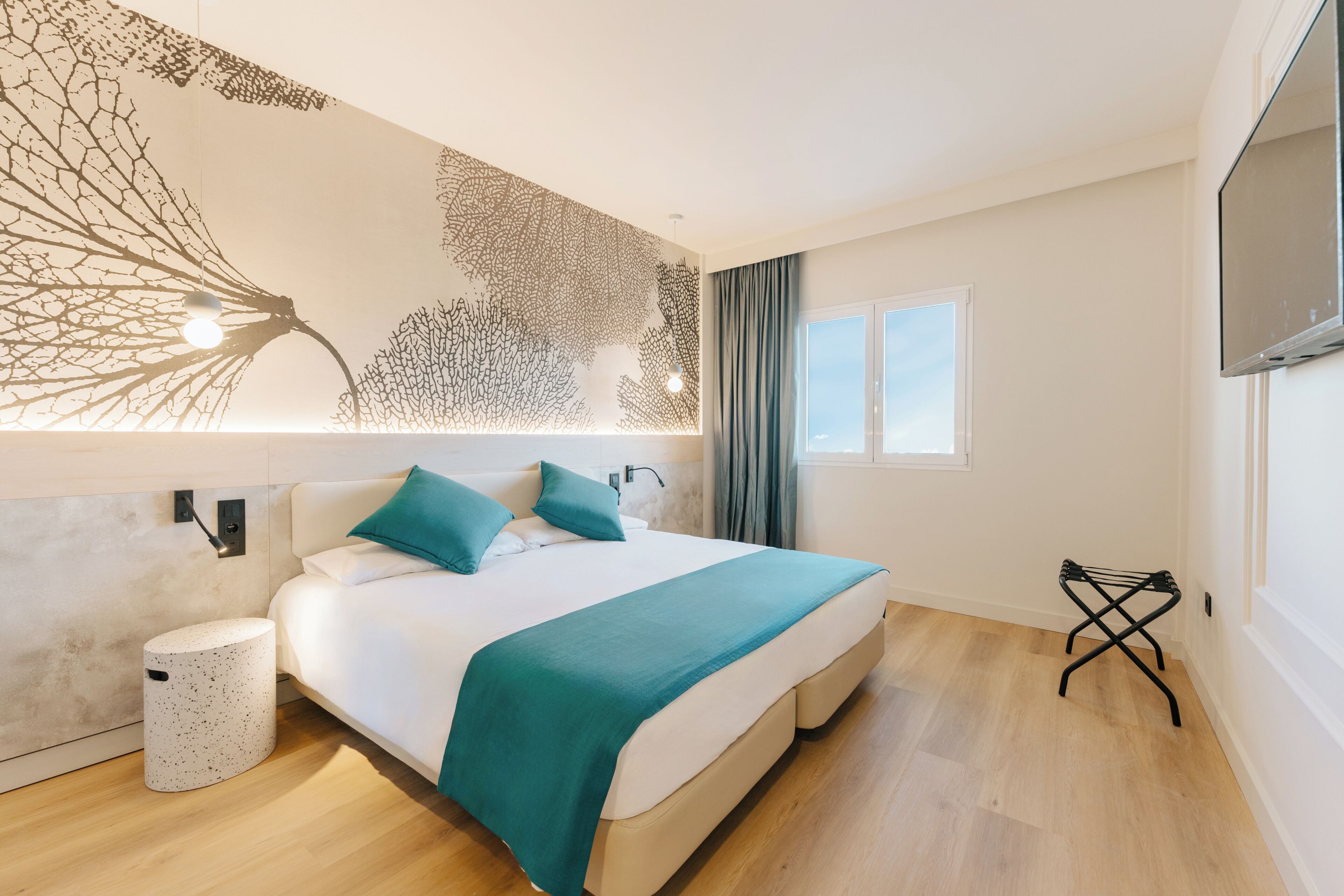 Ein modernes Hotelzimmer mit Bett, Wand-Fernseher, Fenster und Holzboden.