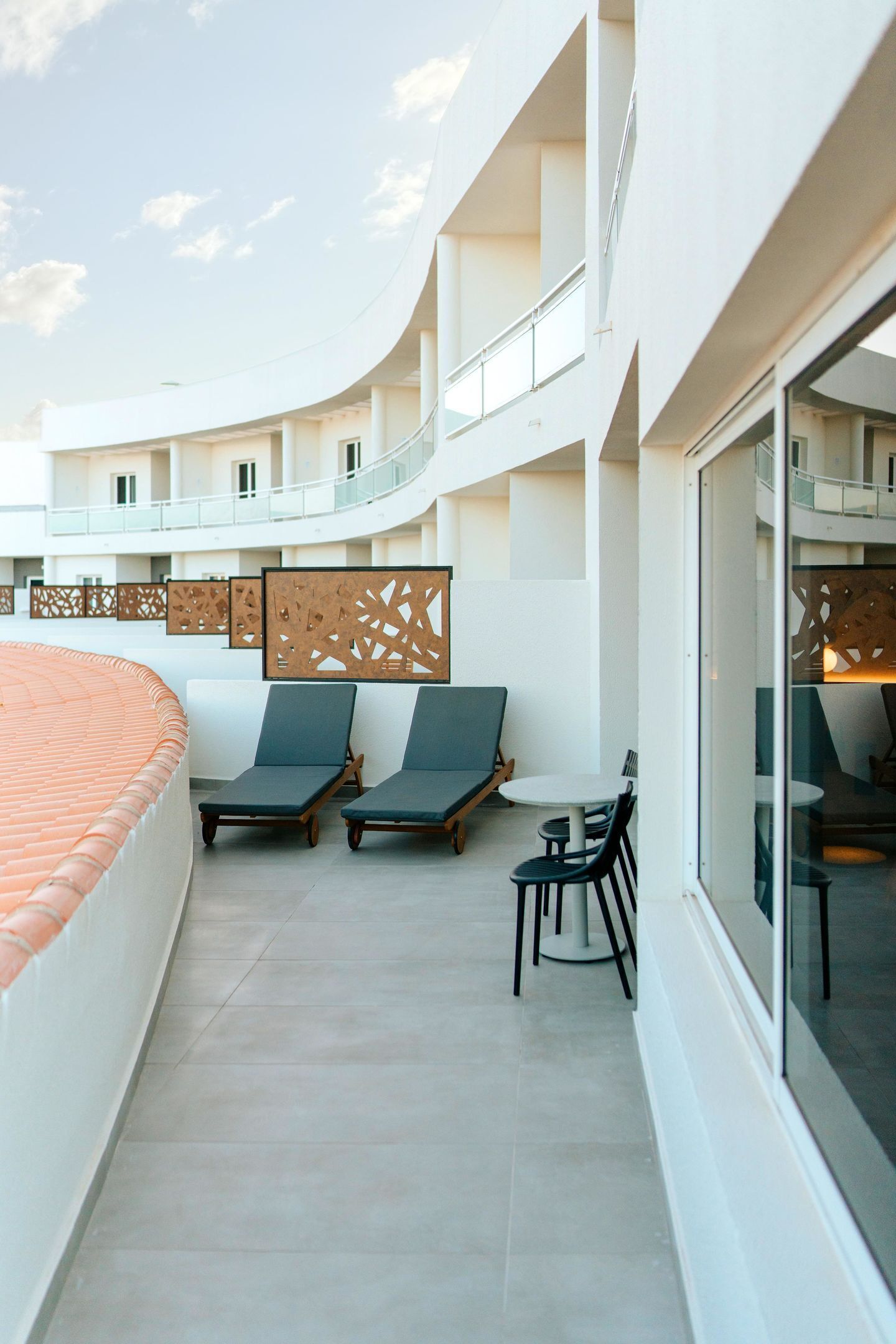 Uma área de estar moderna ao ar livre, com assentos e parede de vidro, parte de um hotel ou resort.
