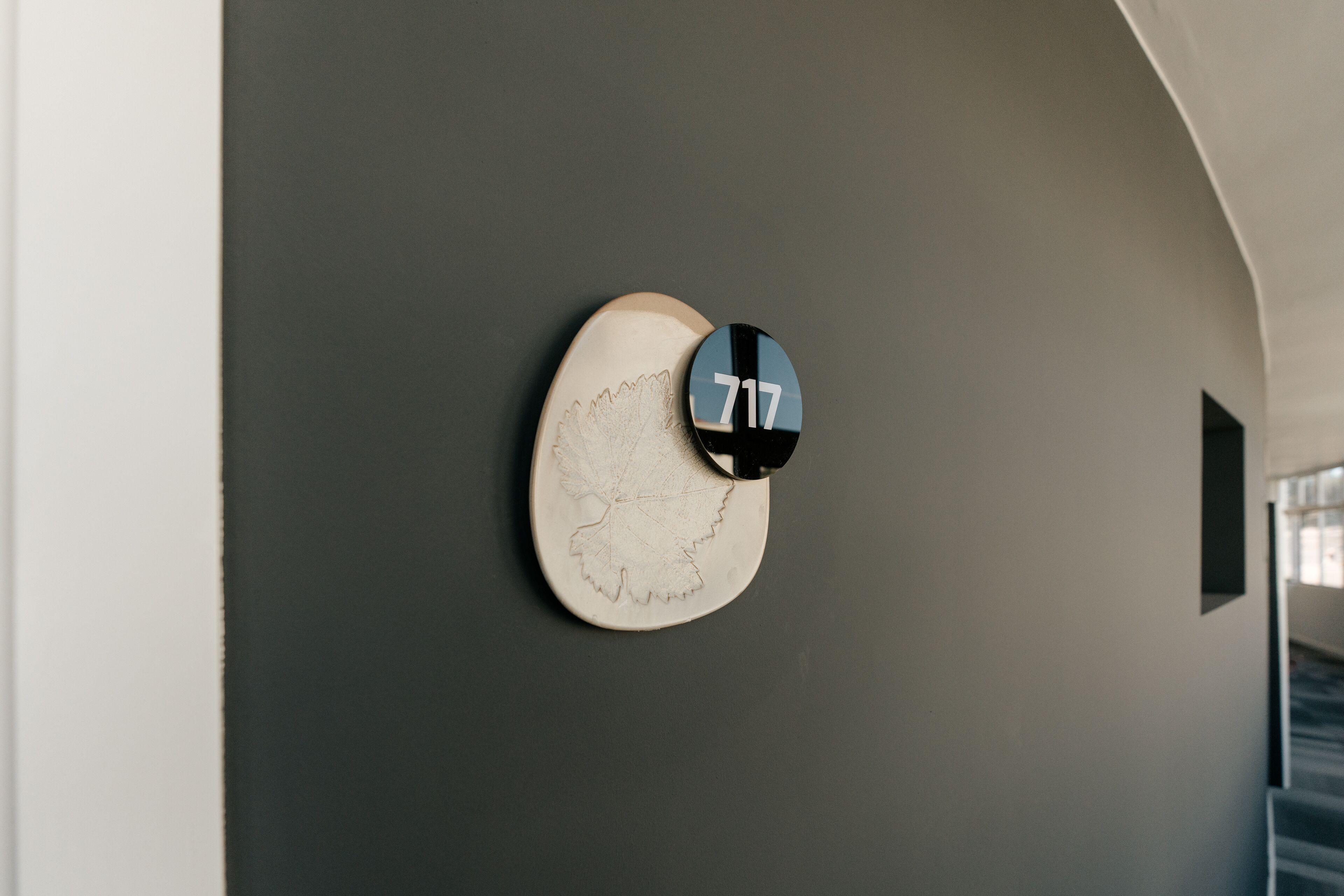Un reloj de pared con diseño original, una pared oscura y una pequeña ventana a la derecha.