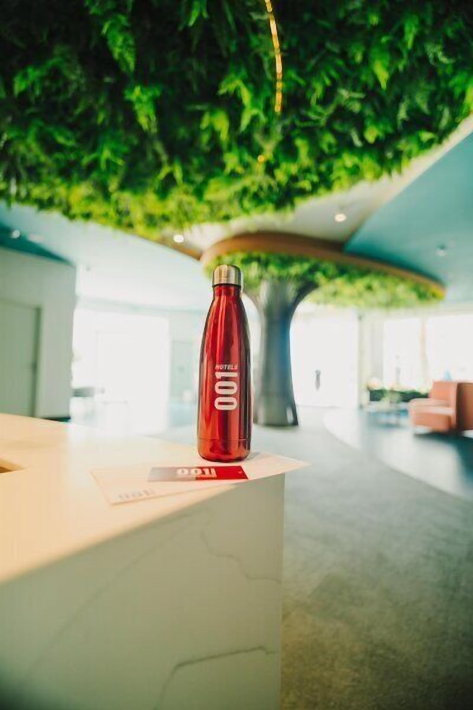 A red water bottle on a white reception desk with a tree in the background.