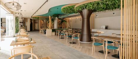 Un restaurant moderne avec de longues tables communes, des chaises en bois et une structure centrale en forme d’arbre.