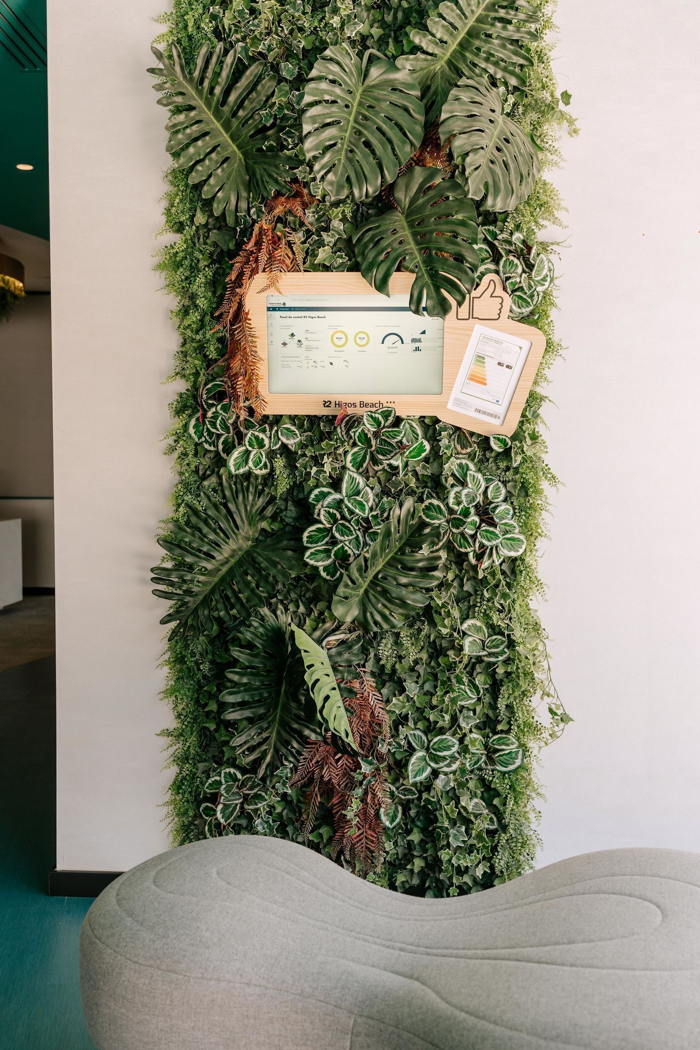 A vertical garden wall with a framed informational display and a gray ottoman.
