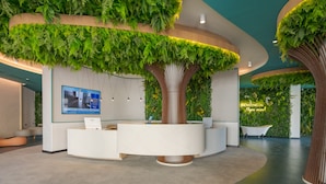 Un espace d’accueil moderne avec un comptoir central, des éléments décoratifs verts sur les murs et une grande structure végétale.