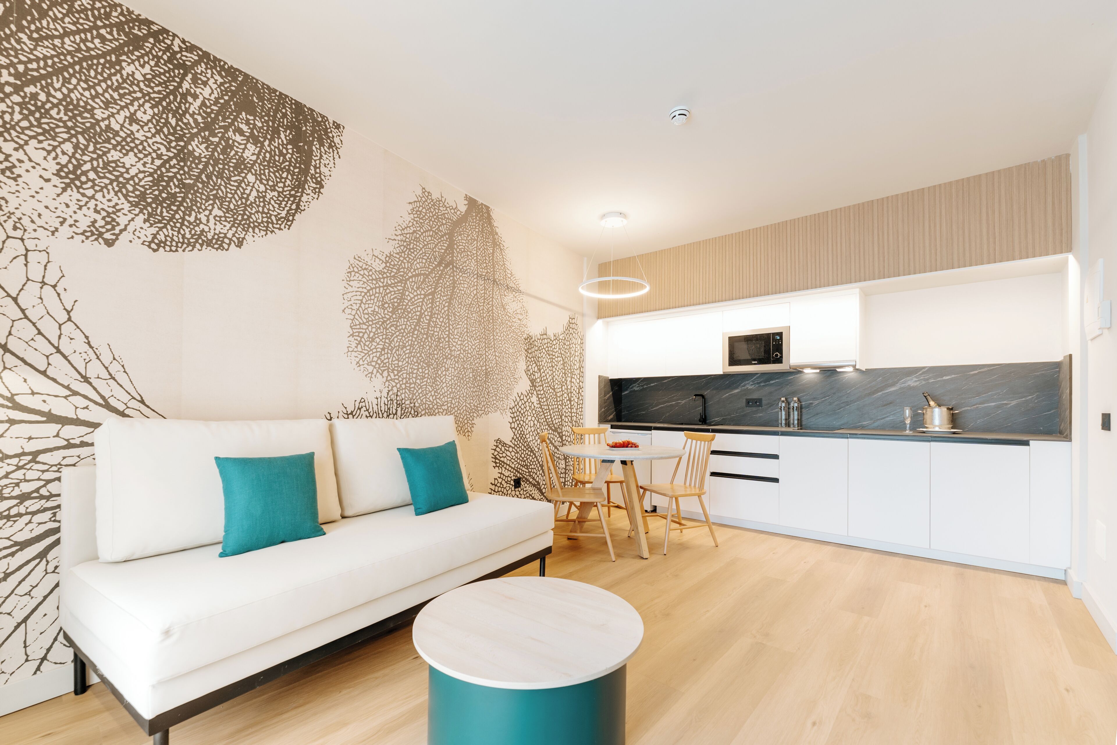 A modern living room with a white sofa, teal cushions, a round coffee table, and a decorative wall piece.