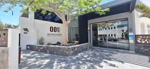 A modern building with a large tree in front, a glass entrance, and the number '001' on the facade. - 001 HIGOS BEACH BOUTIQUE Singular Hotel Residence (Pajara)
