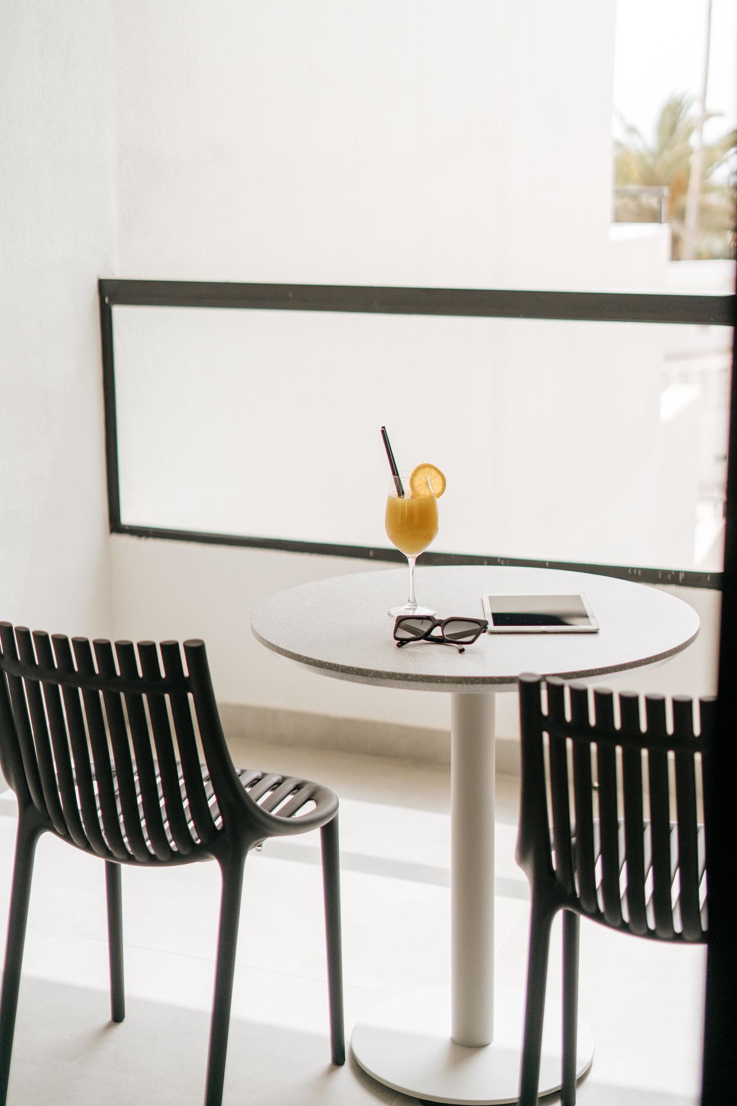A round table with a smartphone and a pair of glasses on it, flanked by two black chairs.