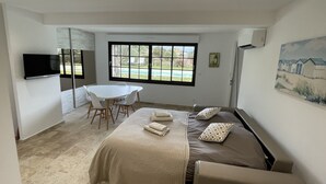 Une chambre à coucher comprenant un lit, un téléviseur, une table à manger avec des chaises et une fenêtre donnant sur une piscine.