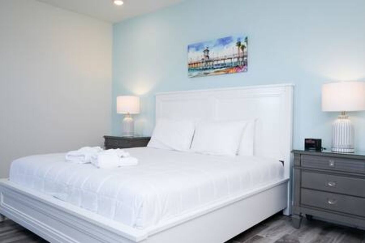 A neatly made bed with white linens, a nightstand with a lamp, and a painting on the wall.