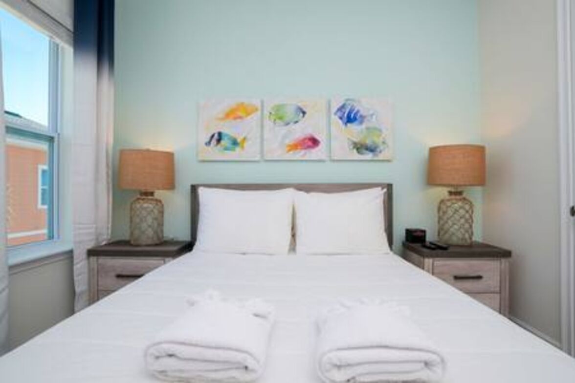 A hotel room with a bed, two bedside tables, a window, and three wall art pieces.