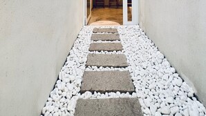 A narrow pathway leading to a room with a bed and two chairs, with a small window and a light fixture on the wall. - RiverChill Inn (Tainan)