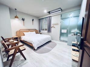 A modern hotel room with a wooden bed, a desk, a chair, a small table, a mirror, and an air conditioning unit.