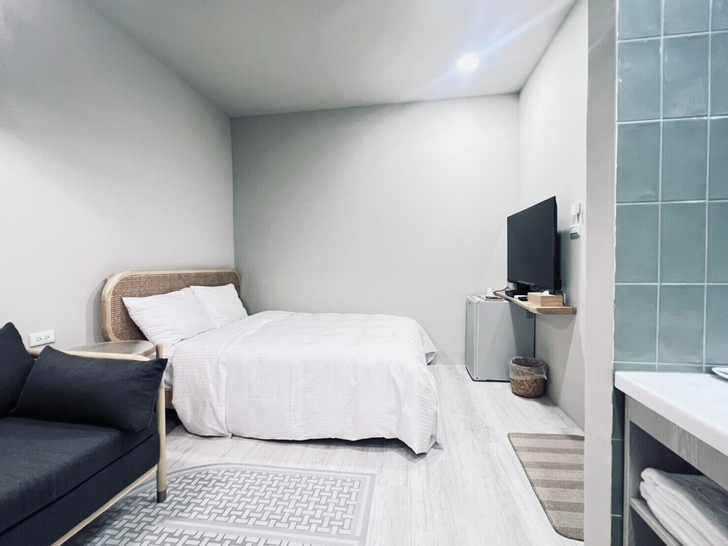 Quarto moderno e minimalista com cama, sofá, televisão e mesa de apoio.
