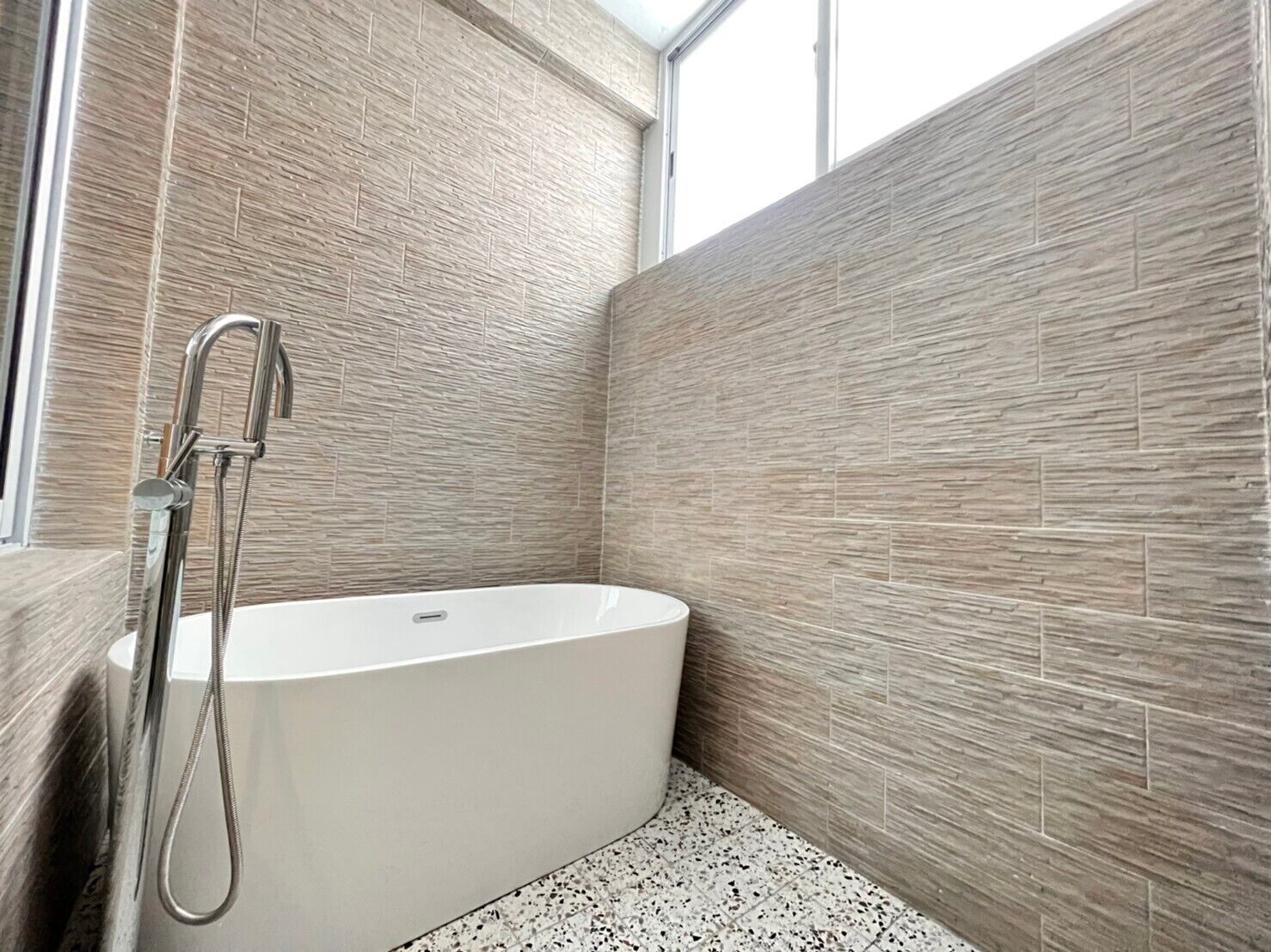 A modern bathroom with a freestanding bathtub, tiled walls, and a window providing natural light.