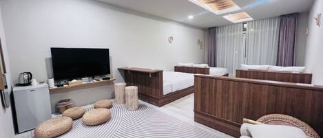A modern hotel room with a large bed, a TV, a small fridge, and a wooden headboard.
