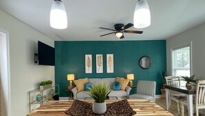 Una sala de estar moderna con una pared de acento color aguamarina, una mesa de comedor de madera y un ventilador de techo.