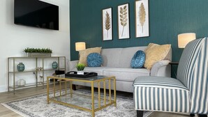 Una sala de estar moderna con una pared de acento color turquesa, un sofá gris, un sillón a rayas y una mesa de centro con marco dorado.