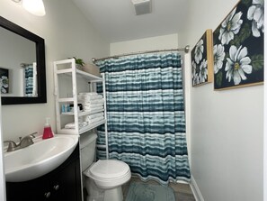 Un baño con lavamanos blanco, inodoro, toallero y cortina de ducha.