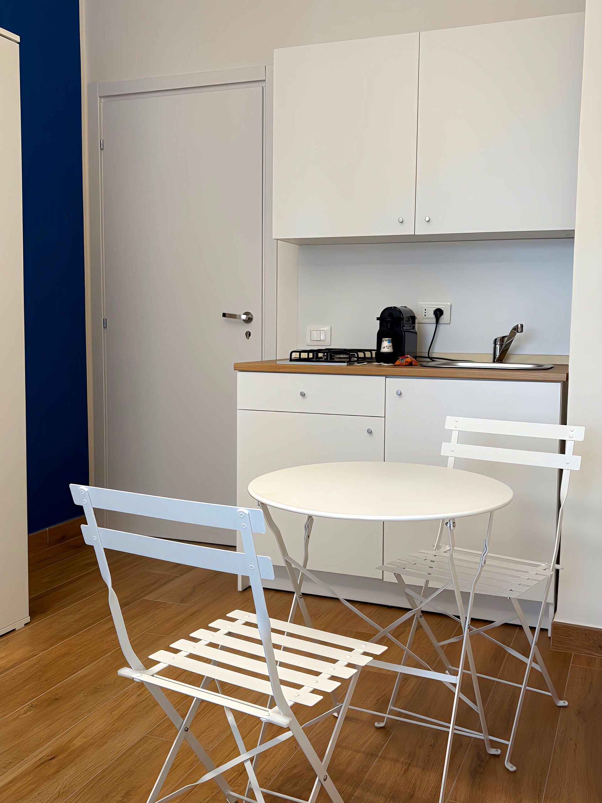A compact kitchen with a white table and chairs, a coffee maker, and a toaster on the counter.