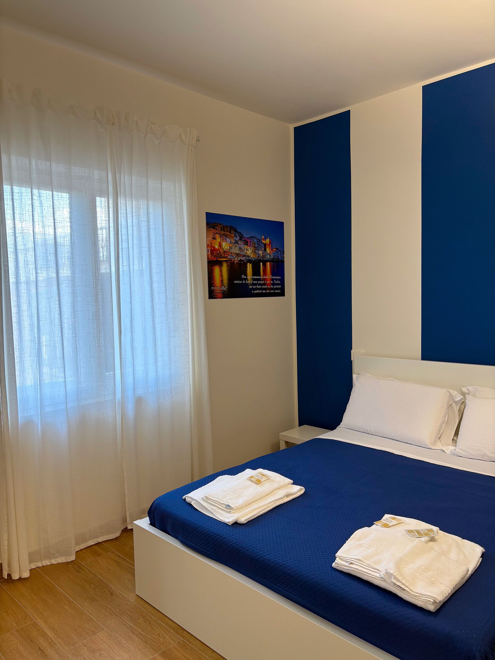 Habitación de hotel con cama, cortinas blancas, un cuadro enmarcado en la pared y una pared de acento azul.