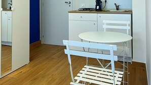 A compact kitchen with white cabinets, a small dining table, and a white chair.