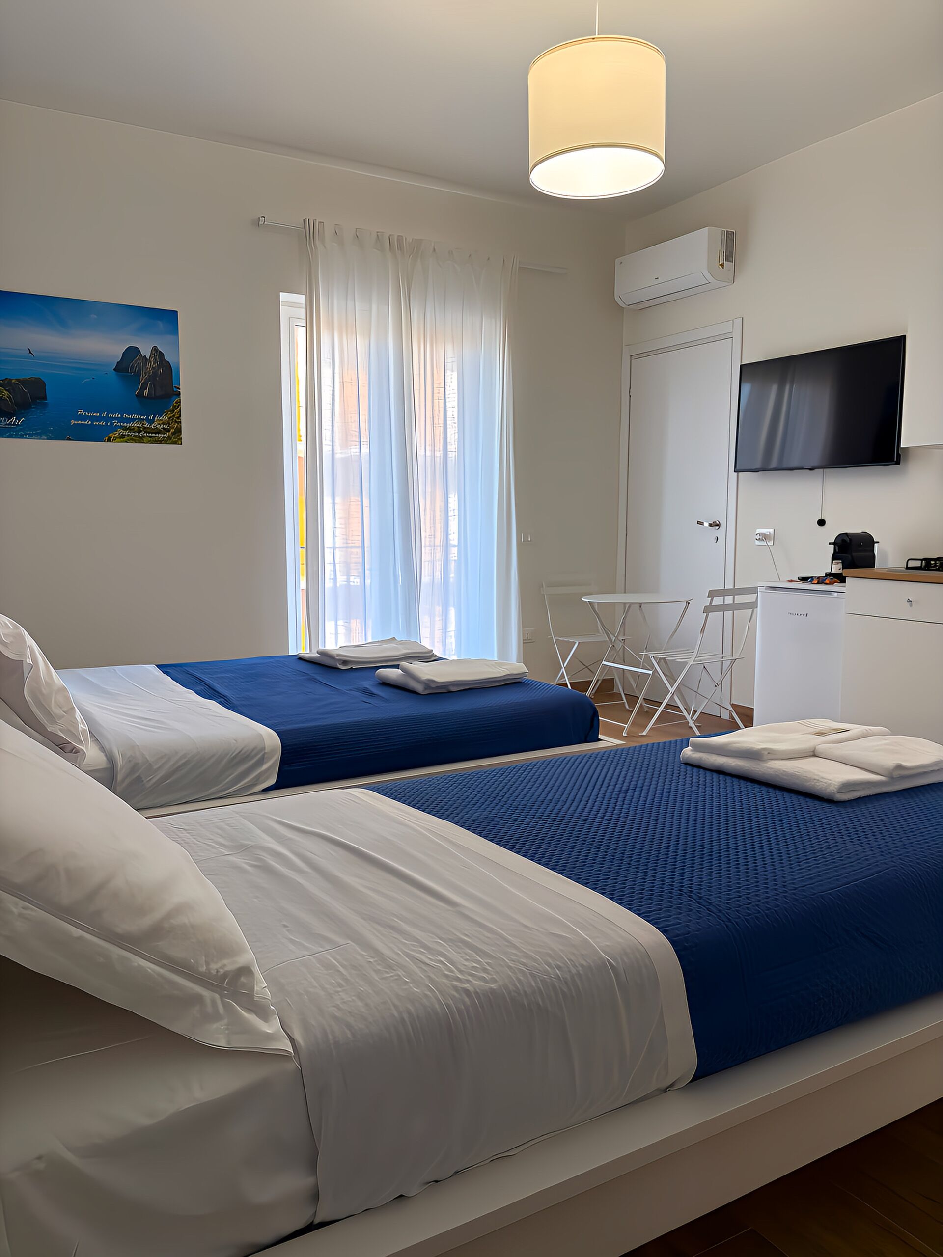 Ein Hotelzimmer mit zwei Betten, einem Fernseher, einer Klimaanlage und einem Gemälde einer Küstenlandschaft.