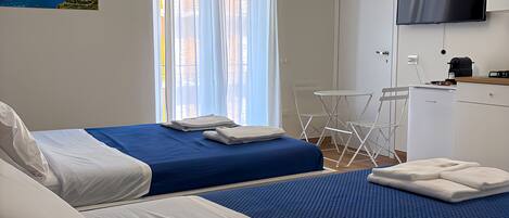 A hotel room with two beds, a TV, an air conditioning unit, and a painting of a coastal scene.