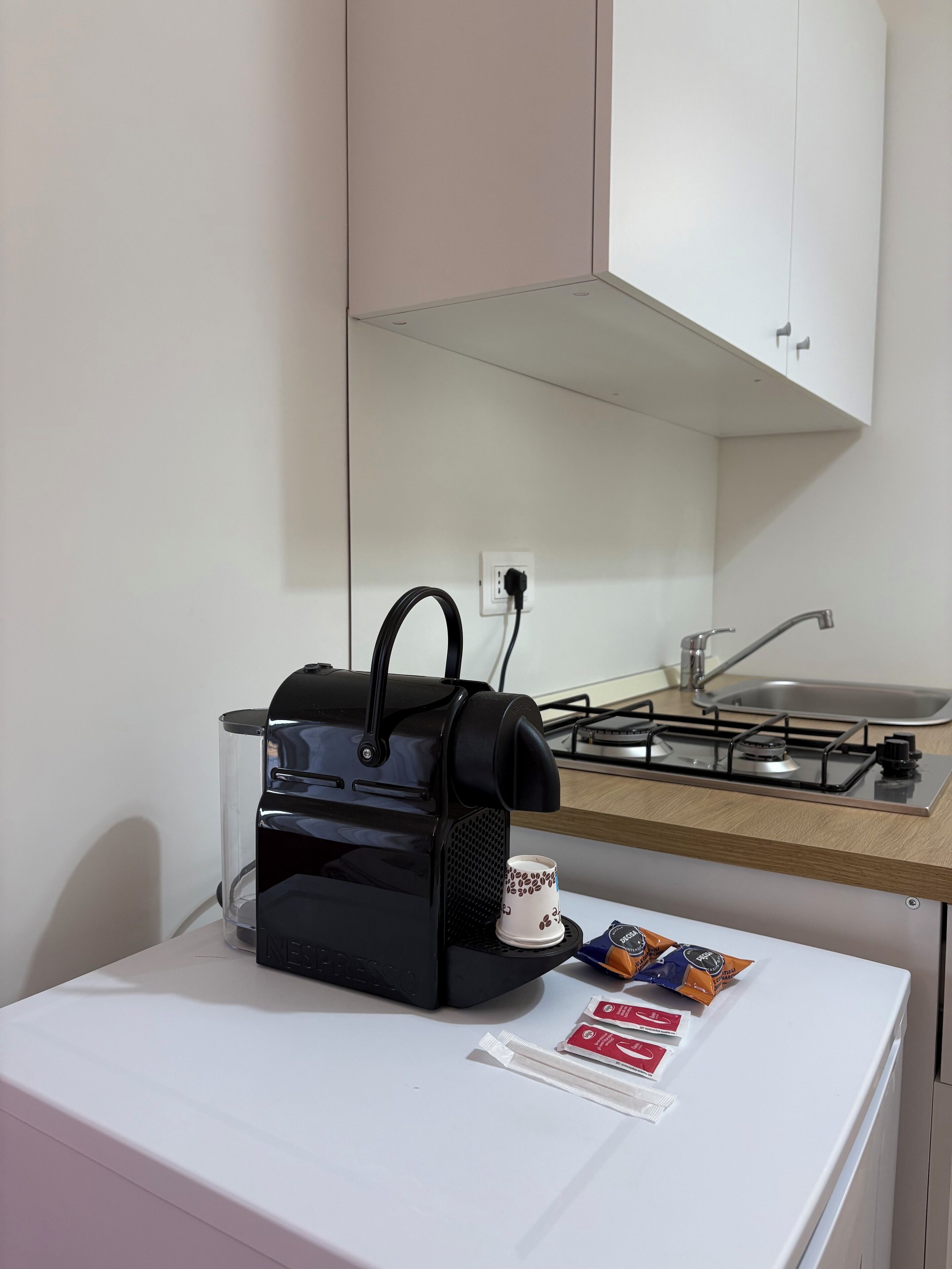 A kitchenette with a coffee maker, a cup, and coffee pods on a white countertop.