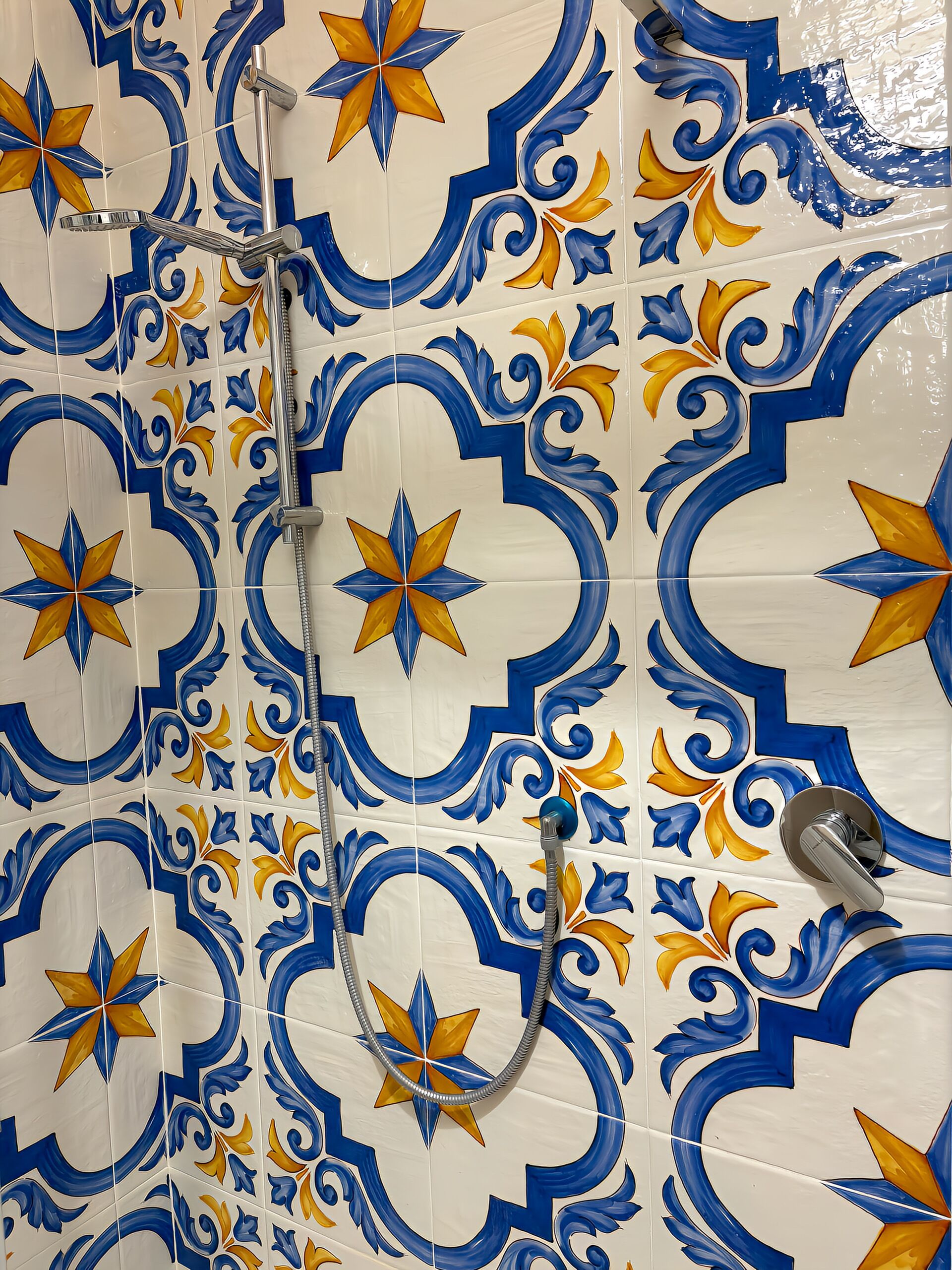 Een badkamer met decoratieve blauwe en gele tegels, een douche met een handdouche en een wandmengkraan.