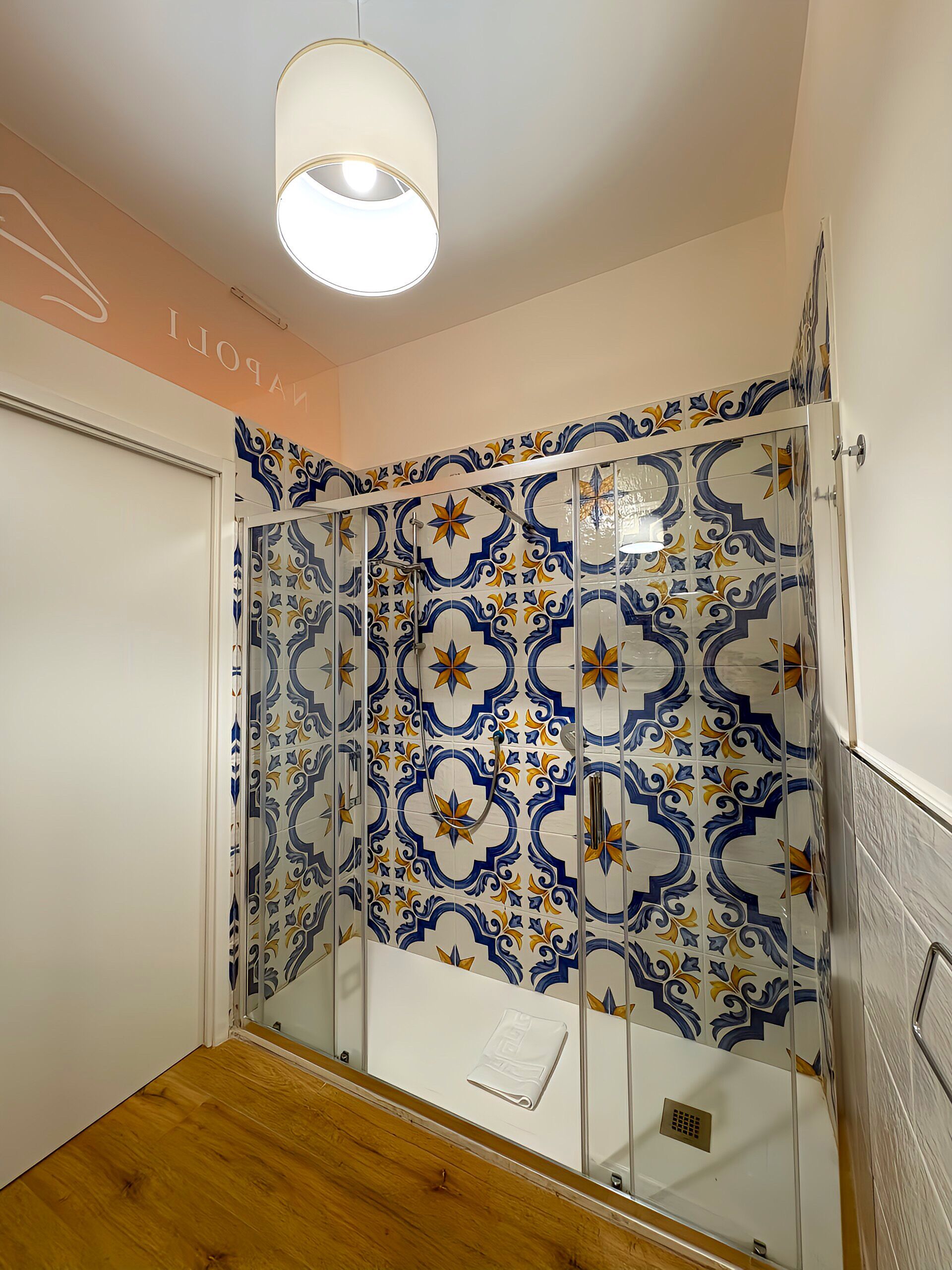 A bathroom with a shower enclosure, patterned tiles, and a wooden floor.