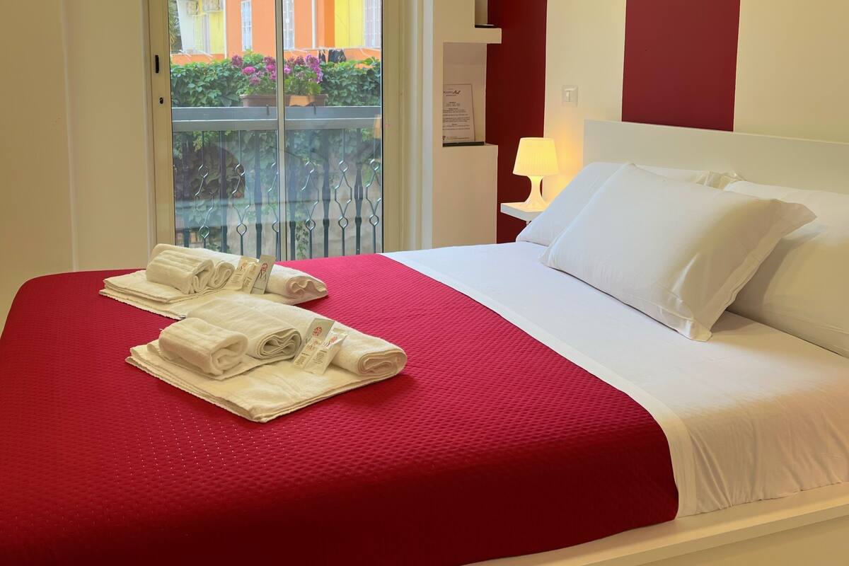 A hotel room with a bed, red bedding, white pillows, and a red wall.
