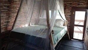 Ein Einzelbett mit Moskitonetz in einem Raum mit Steinwänden und einer Holztür.