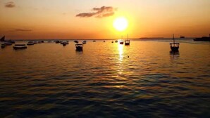 Ein Sonnenuntergang über einem ruhigen Meer mit mehreren vor Anker liegenden Booten.