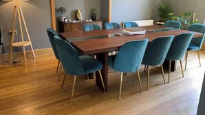 Un salón de conferencias con una mesa de madera, sillas color esmeralda, una lámpara de pie y una planta en maceta.