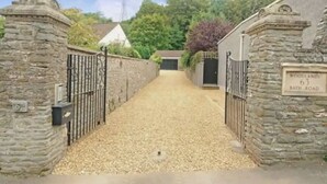 Un camino de grava conduce a una entrada con puerta de reja, muros de piedra y un letrero que muestra el número 63 de Bath Road.