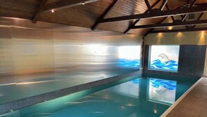 Una piscina interior con agua cristalina, un solárium con baldosas y un mural de delfines en la pared.