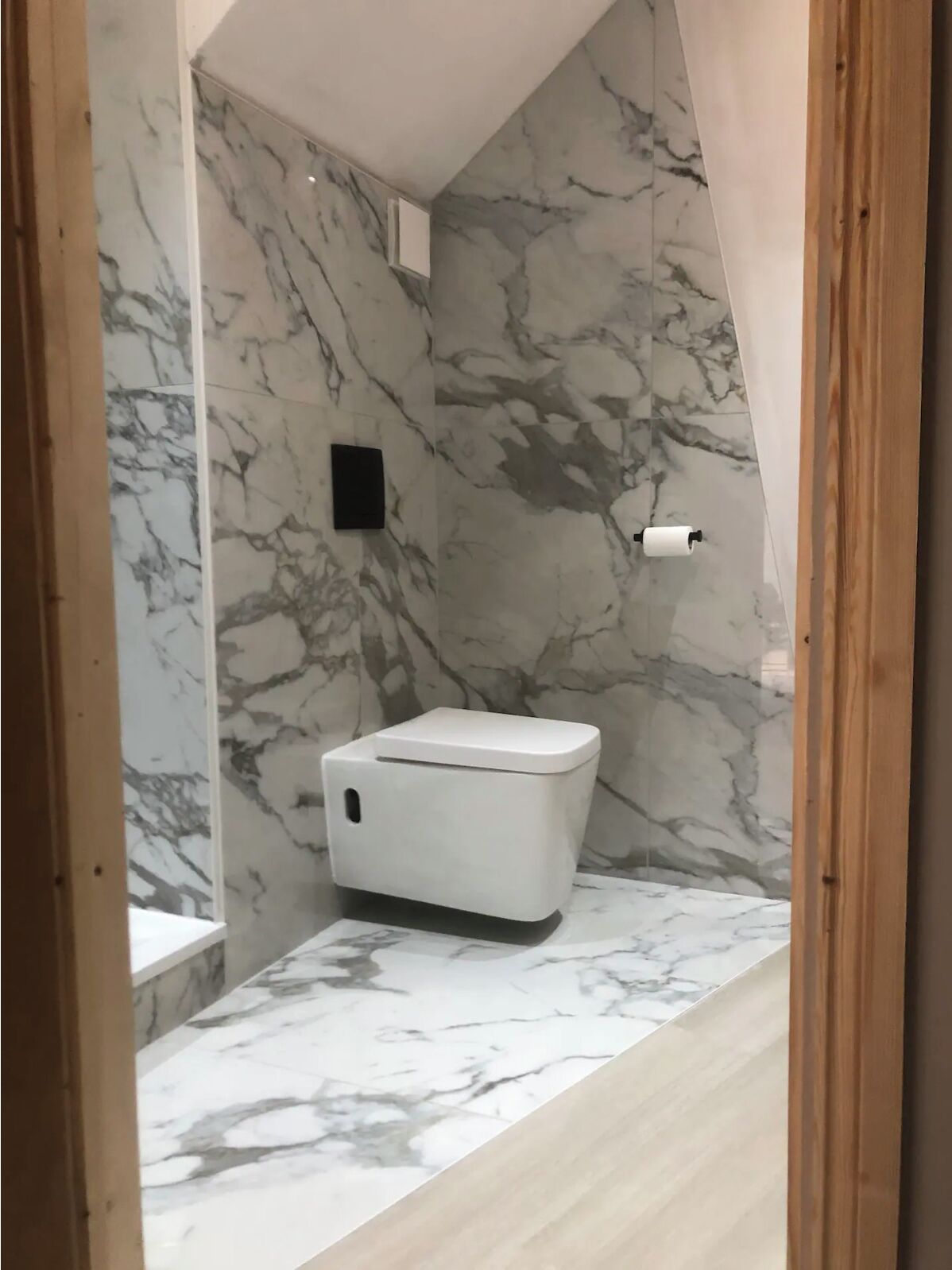 Ein Badezimmer mit Toilette, Marmorwänden und Holzboden.