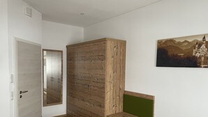 Ein Schlafzimmer mit einem Holzschrank, einem Bett mit einem Bettschlupf in Rautenmuster, einer grünen Bank und einem Wandbild mit einer Burg.