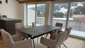 Ein Essbereich mit Tisch und Stühlen, große Fenster mit Blick auf schneebedeckte Berge.