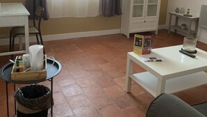 Ein Wohnzimmer mit einem weißen Schrank, einem kleinen Tisch, einem Sessel und einem Fenster mit Vorhängen.