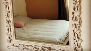 Ein Bett mit weißer Bettdecke und einem rosafarbenen Kopfkissen, eingerahmt von einem aufwendigen weißen Spiegel.