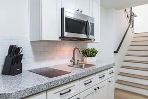 Kitchen features a granite countertop, stainless steel sink, and microwave, with a staircase nearby.